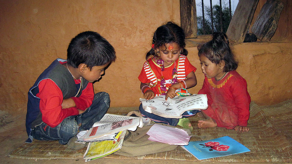 Three children read a book while pointing at the pictures.